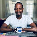 Portrait of a smiling man sitting indoors with a coffee mug in Nairobi, Kenya.