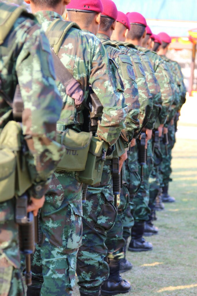 A group of soldiers in camouflage uniforms with berets line up outdoors, holding rifles.